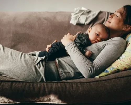 Woman resting on the couch with her baby laying on her chest